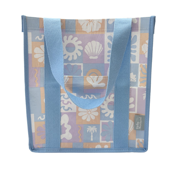 A square canvas tote bag with a pastel patchwork pattern featuring seashells, flowers, and palm trees in lavender, orange, and light blue, with solid light blue handles.  Lizzie Print - Daily Bag - Reusable bags online | Weekender bags | Shopper bags | Pouches  Hello Weekend Beige canvas handles | Beach Bags