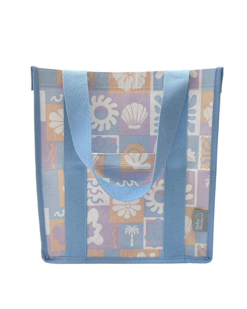 A square canvas tote bag with a pastel patchwork pattern featuring seashells, flowers, and palm trees in lavender, orange, and light blue, with solid light blue handles.  Lizzie Print - Daily Bag - Reusable bags online | Weekender bags | Shopper bags | Pouches  Hello Weekend Beige canvas handles | Beach Bags