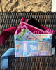 A small zippered pouch with a maroon wrist strap, featuring a palm tree and sun mixed pattern of bright pink shapes on a maroon colour. A small fabric tag on the right reads Hello Weekend. Layla Print - Phone Pouch - Reusable bags online | Daily bags | Shopper bags | Weekender bags  Hello Weekend