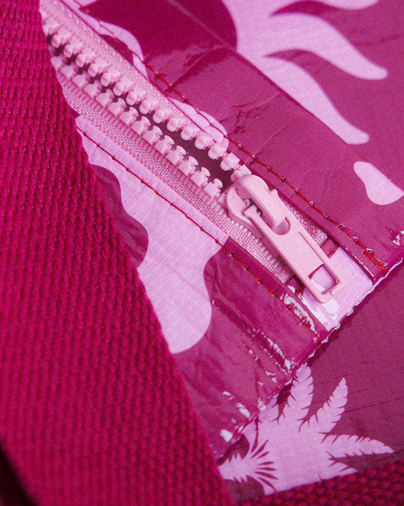 A small zippered pouch with a maroon wrist strap, featuring a palm tree and sun mixed pattern of bright pink shapes on a maroon colour. A small fabric tag on the right reads Hello Weekend. Layla Print - Phone Pouch - Reusable bags online | Daily bags | Shopper bags | Weekender bags  Hello Weekend