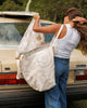 Person with a patterned tote bag standing next to a vintage car. Sandy Print - Weekender Bag - Reusable bags online | Daily bags | Shopper bags | Pouches  Hello Weekend Beige canvas handles | Beach Bags